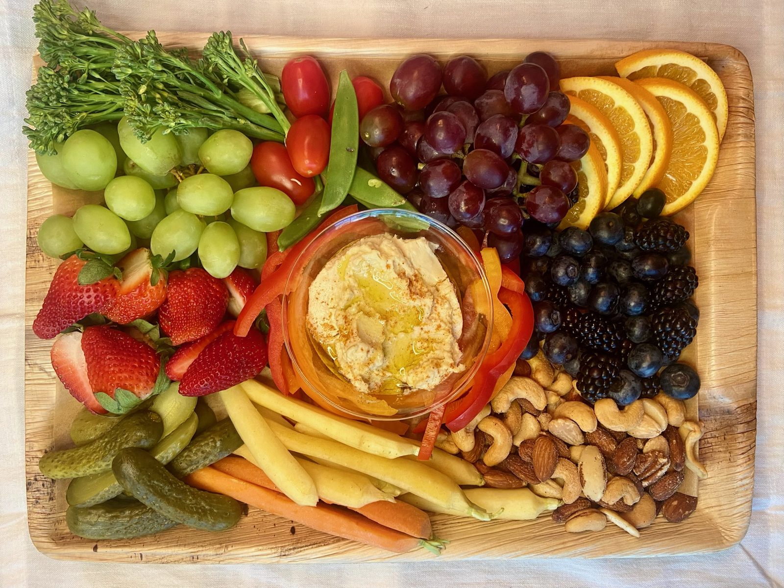 Rectangular board with hummus, crudités, citrus, and berries